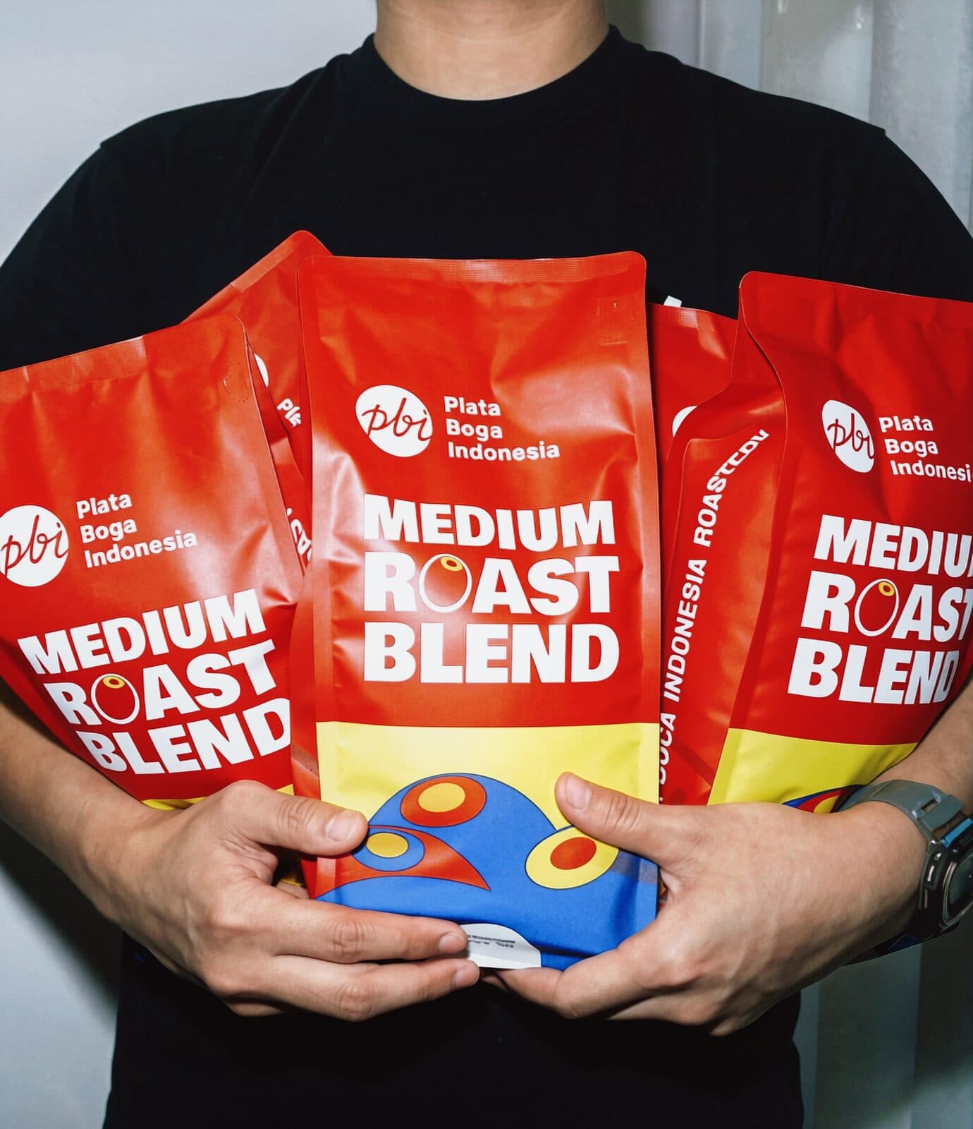 Tiga kemasan Medium Roast Blend dipegang di depan dada